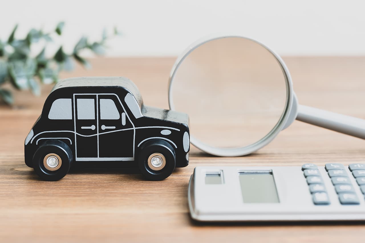 木製の黒い車の模型と、その横に置かれた虫眼鏡、手前にある電卓。