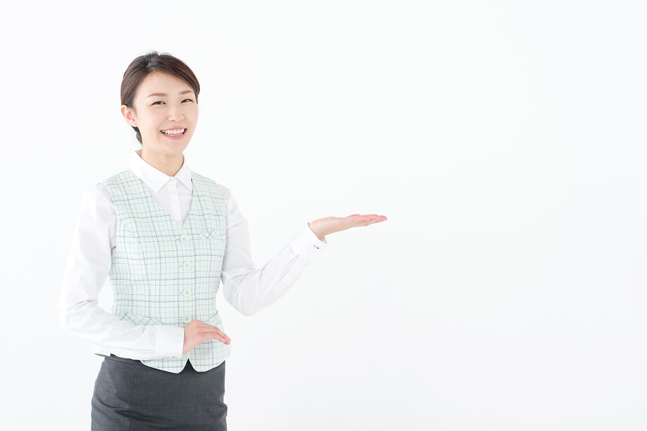 笑顔で左手を差し出し案内ポーズをとる制服姿の女性スタッフ。