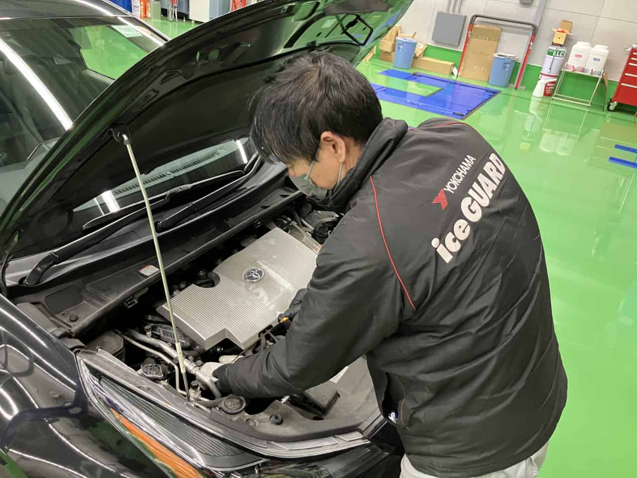 車のボンネットを開け、エンジンルーム内を点検・整備するメカニックの男性。