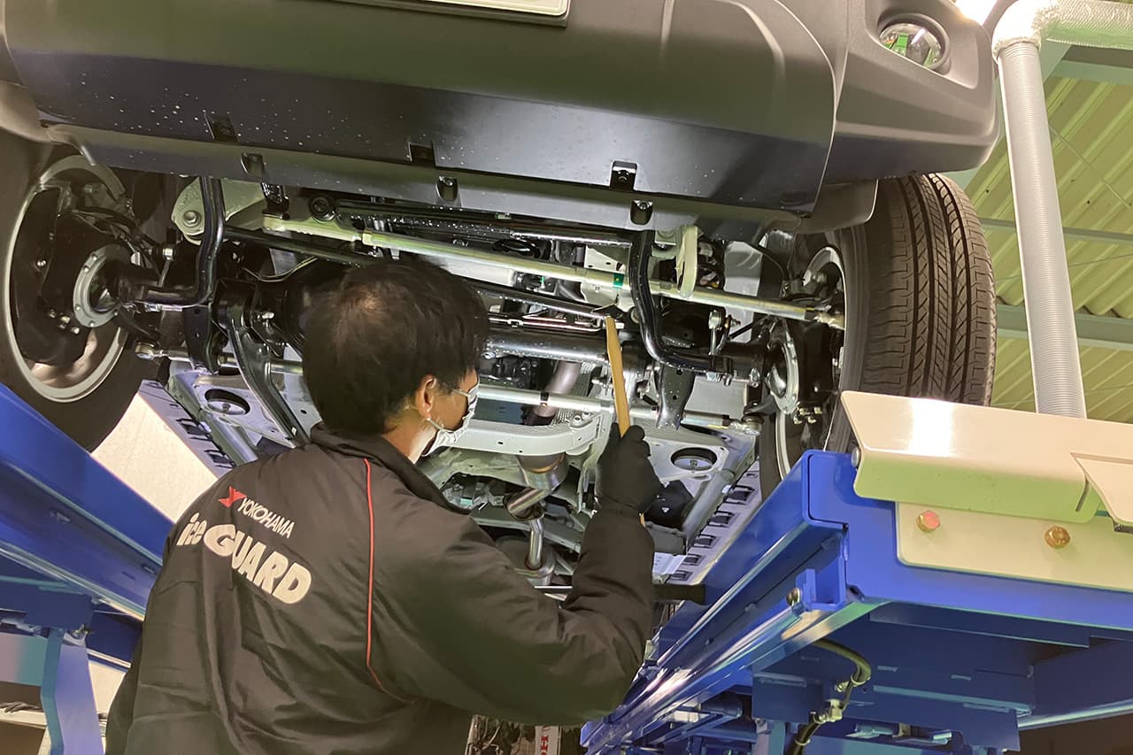 リフトで持ち上げられた車を整備する整備士の様子